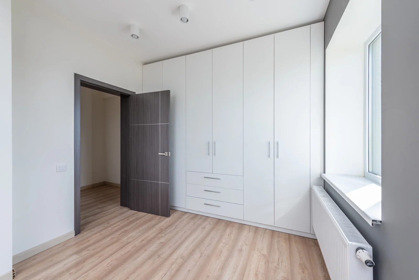 A wall of white slab fitted wardrobes in a bedroom